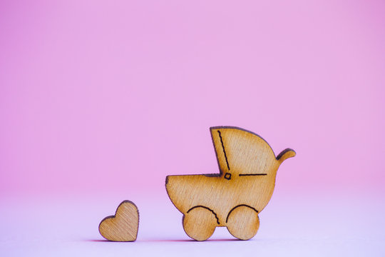 Wooden icon of baby buggy and little heart on pink background