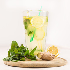 A glass decanter with a summer refreshing lemonade made of lemons and ginger with mint added on a...