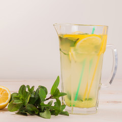 A glass decanter with a summer refreshing lemonade made of lemons and ginger with mint added on a white wooden background. Detox water. Ingredients. Cleaning the body of toxins, vitamins