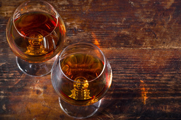Two snifter wine glasses with cognac or brandy on vintage wooden background. Top view. Copy space for text. 