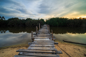 Obraz premium The old wooden bridge over a river at Kg. Pulau Kerengga, Marang Malaysia with sunset scenery