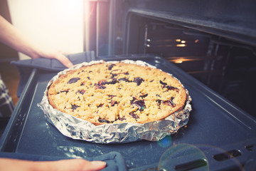 Woman hands taking out tray with pastry from oven, closeup. Fresh homemade delicious plum pie.