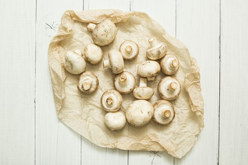 Farmer's mushrooms champignons on parchment paper. Organic vegetables on a white wooden background.