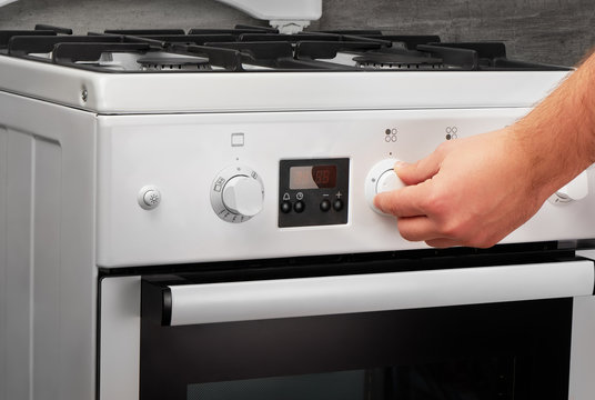 Male hand turning on white stove on gray background