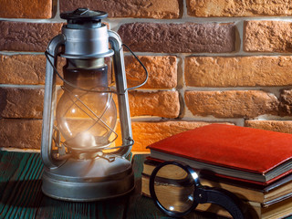 Obraz na płótnie Canvas Still life kerosene lamp shines on wooden desktop stone brick background book camera.