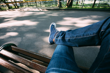 First-person view a man sitting on wooden bench in the park. - Powered by Adobe