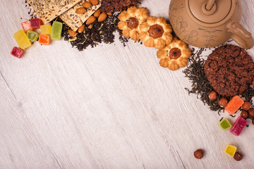 The composition of the tea on a wooden surface. brown teapot from clay with a scattering of tea, almond and hazelnut. Green, black tea. Cookies and gummy candies. Top view with copy space.
