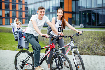 Fototapeta na wymiar Young parents ride a bicycle with a small daughter on city streets