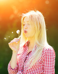 Beautiful young woman blowing seeds from a flower dandelion