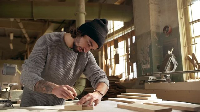Concentrated multi-ethnic male with black beard dimensioning wooden workpiece in joinery for further work with it. Footage in slowmotion