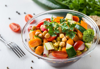 Vegetable salad in glass bowl with broccoli and tomatoes on white table.