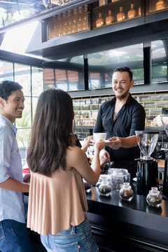 Cheerful bartender serving coffee over the bar counter to a young female customer
