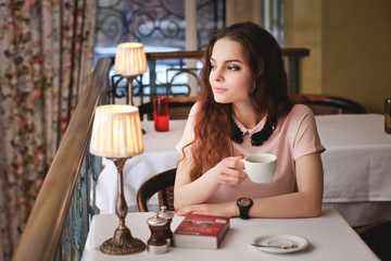 Beautiful young girl sitting alone in a cafe, drinks coffe and h