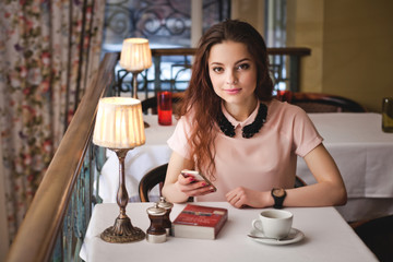 Beautiful young girl sitting alone in a cafe, drinks coffe and u