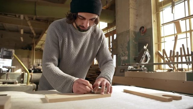 Young multi-ethnic male with black beard dimensioning wooden detail for further work in joinery. Footage in slowmotion