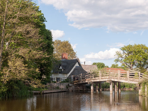 the bridge at flatford mill leading to a cottage in the heartland of constable country essex and suffolk near Dedham with people on the bridge viewing on a sunny relaxing afternoon