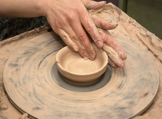 Woman hands in clay at process of making clay bowl on pottery wheel