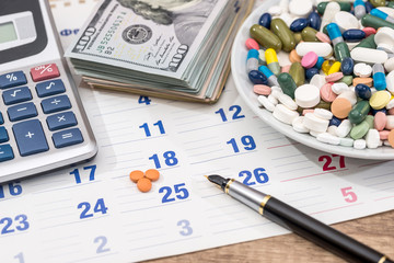pills and dollar, pen, calculator on calendar.