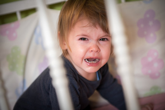 Close-up portrait of crying baby in crib at home