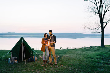 Man and woman lovers hold a flashlight at dawn near the lake