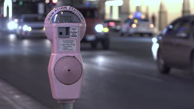 Street parking meter with cars driving by in evening.
