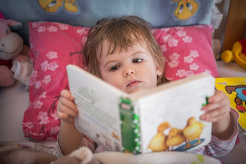 Cute little girl reading in bed