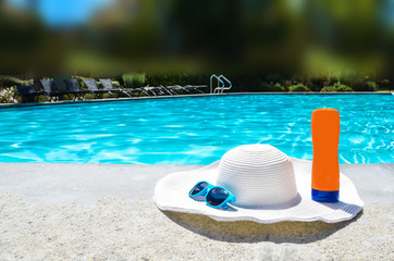 Fototapeta na wymiar Summer hat, sunglasses and sunscreen near the pool