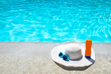 Naklejka premium Summer hat, sunglasses and sunscreen near the pool