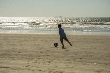 menino jogando futebol na praia