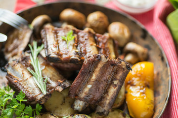 Ribs grilled in a frying pan with rosemary and mushrooms on a table