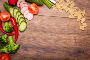 tomato, radish, cucumber, broccoli, onion, chili, pasta, macaroni on a wooden surface. arrangement of sliced vegetables. Top view with copy space for text