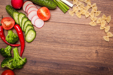 tomato, radish, cucumber, broccoli, onion, chili, pasta, macaroni on a wooden surface. arrangement of sliced vegetables. Top view with copy space for text © deminitry8