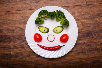 the vegetables on the plate in the form of a smile on a wooden surface. the view from the top.