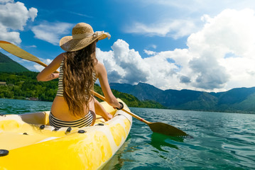 Beautiful young woman with long hair and hat paddling on lake
