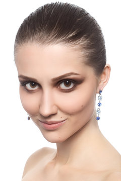 Portrait of young beautiful female with evening makeup and earrings looking at camera on white background