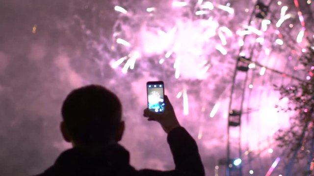 Slowmotion of closeup silhouette of man watching and photographing fireworks explode on smartphone camera outdoors