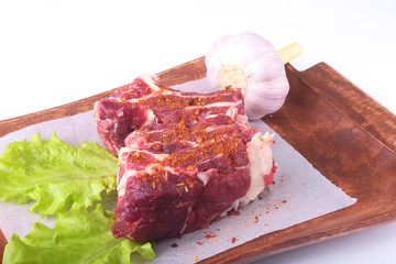 Raw beef edges, lettuce leaf, garlic, pepper grinder and spices on wooden desk isolated on white background from above and copy space. ready for cooking.