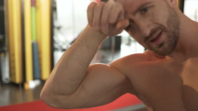 Sporty guy flexing muscles and looking at bicep, catching breath after exercise
