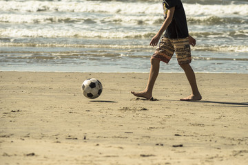 menino jogando futebol na praia