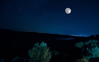 Fototapeta na wymiar Mountain Road through the forest on a full moon night. Scenic night landscape of dark blue sky with moon. Azerbaijan. Long shutter photo