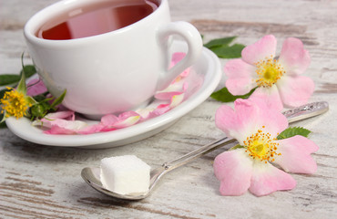Fototapeta na wymiar Cup of tea and wild rose flower on rustic wooden background
