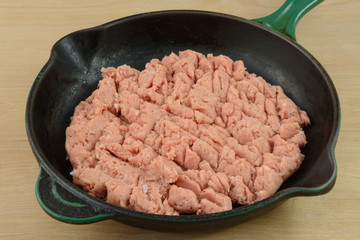 Raw ground turkey meat in cast iron frying pan in preparation for cooking