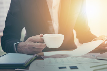 Young businessman in a black  jacket with a cup of coffee, reading a document report