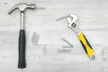 A silver hammer, a wrench, several screw bolts and dowels on light wooden background.