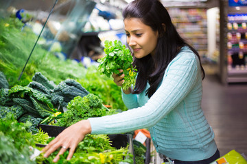 Closeup portrait, beautiful, pretty young woman in sweater picking up, choosing green leafy vegetables in grocery store