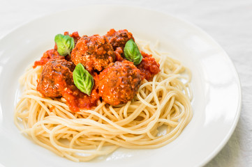 Spaghetti pasta with meatballs in tomato sauce and basil leaves against white background
