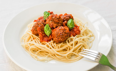 Spaghetti pasta with meatballs in tomato sauce and basil leaves against white background
