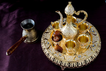 Still-life with traditional golden Arabic coffee set with dallah, coffee pot and dates. Dark background. Horizontal photo