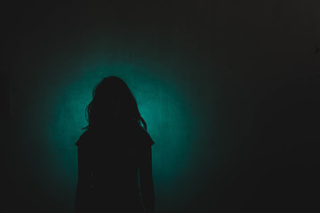 silhouette of depress woman standing in the dark with light shine behind