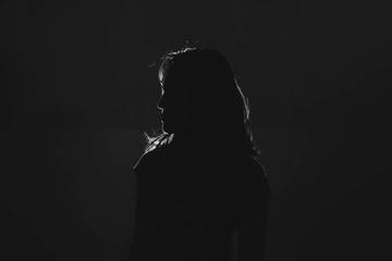 silhouette of depress woman standing in the dark with light shine behind - Powered by Adobe